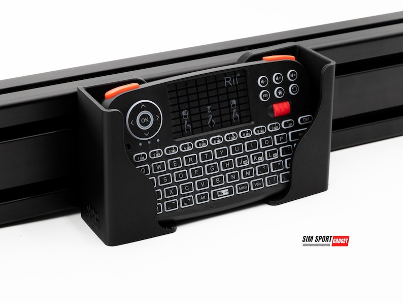 Puede incluir: Un mini teclado negro con teclas blancas y detalles en naranja est&aacute; montado en un marco negro. El teclado tiene un panel t&aacute;ctil y botones de funci&oacute;n. La marca "Rii" es visible.
