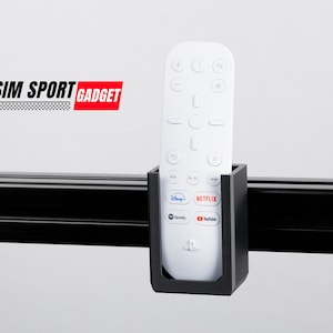 May include: A white remote control with black buttons is held in a black plastic holder mounted on a black metal track. The remote has buttons for TV, Netflix, Disney+, YouTube, Spotify, and PlayStation. The text "SIM SPORT GADGET" is visible in the background.
