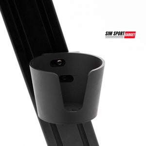 Puede incluir: Portavasos negro unido a un marco de metal negro. El portavasos está diseñado para sostener una bebida. El texto "SIM SPORT GADGET" es visible en la esquina superior derecha de la imagen.