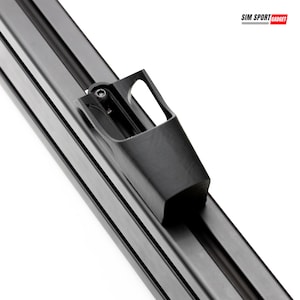 May include: Close-up of a black, rectangular component with a small, angled bracket attached. The component has a series of parallel grooves and a small, rectangular opening. The text "SIM SPORT GADGET" is in the upper right corner.