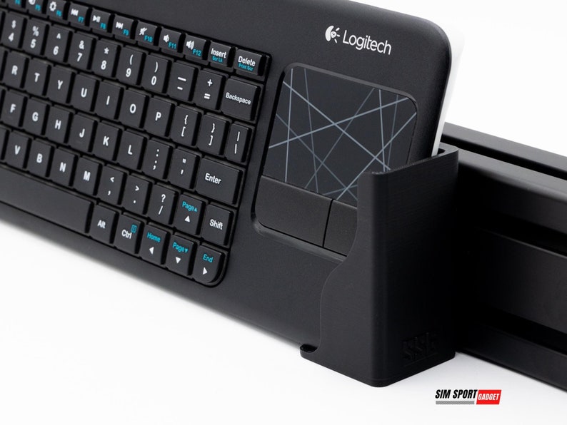 Puede incluir: Teclado inal&aacute;mbrico Logitech negro con panel t&aacute;ctil integrado. El teclado tiene un dise&ntilde;o QWERTY completo con teclas de funci&oacute;n y teclado num&eacute;rico. El panel t&aacute;ctil presenta un dise&ntilde;o geom&eacute;trico. El teclado se muestra en un soporte negro.