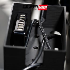 Pode incluir: Uma caixa de pl&aacute;stico preta com um hub USB no interior. A caixa tem o texto "SIM SPORT GADGET" impresso na parte superior.
