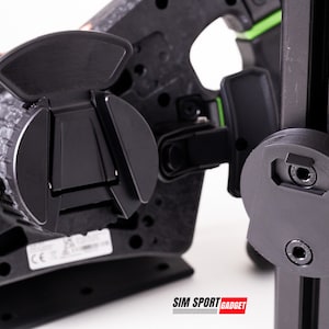 Könnte beinhalten: Nahaufnahme einer schwarzen Metallhalterung mit Schnellverschlussmechanismus. Die Halterung ist an einem schwarzen Metallpfosten mit grünem Streifen befestigt. Der Text "SIM SPORT GADGET" ist auf dem Pfosten sichtbar.