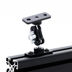 May include: Black metal camera mount with a swivel arm and a flat plate with three holes. The mount is attached to a black metal track.