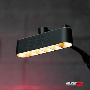 May include: A black rectangular light fixture with the letters "GGG" on the front. The fixture has six triangular light panels that emit a warm, golden glow. The fixture is mounted on a black arm.