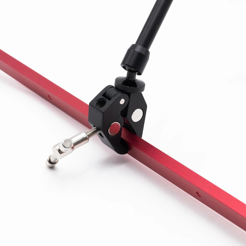 May include: A black clamp with a red button attached to a red metal bar. The clamp has a silver knob and a black arm extending upwards.