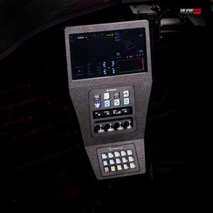 May include: A black textured sim racing dashboard featuring a top-mounted digital display screen, a central control panel with four circular knobs, and a lower Stream Deck unit with a grid of illuminated buttons. The text SIM SPORT GADGET is visible.