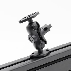 May include: Black adjustable ball mount with a textured surface and a slotted handle. The mount is attached to a black rail with screws. The mount is designed to hold a device.