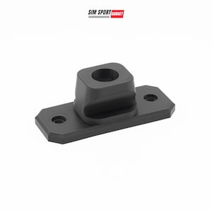 May include: A matte black mounting bracket featuring a rectangular base with two countersunk screw holes and a central raised cylindrical housing with a circular opening. The text SIM SPORT GADGET is printed in black and red above the object.