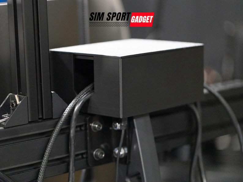 Pode incluir: Uma caixa de pl&aacute;stico preta com um recorte para cabos, montada em uma estrutura de metal preta. A caixa est&aacute; etiquetada com "SIM SPORT GADGET".