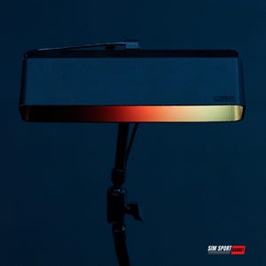 Op de afbeelding: Een rechthoekige, donkerblauwe lamp met een goudkleurige rand en een gradiënt van rood naar geel licht. De lamp is gemonteerd op een zwarte standaard. Het woord "GONGEE" staat op de lamp.