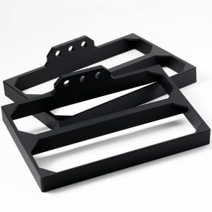 May include: Two black metal rectangular frames with a geometric design. Each frame has a series of three holes on one side. The frames are stacked on top of each other, with the top frame slightly offset.