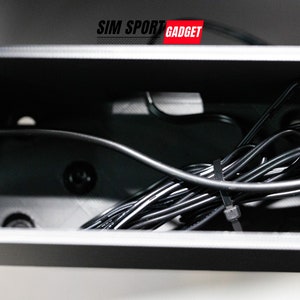 Pode incluir: Uma caixa de pl&aacute;stico preta com um cabo preto dentro. O cabo &eacute; fixado com um amarrilho de pl&aacute;stico preto. A caixa tem o texto "SIM SPORT GADGET" na parte superior.