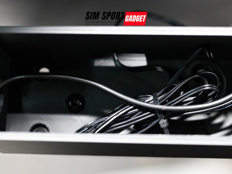 Pode incluir: Uma caixa de pl&aacute;stico preta com um cabo preto dentro. O cabo &eacute; fixado com um amarrilho de pl&aacute;stico preto. A caixa tem o texto "SIM SPORT GADGET" na parte superior.