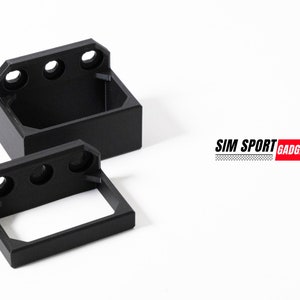 May include: Two black plastic brackets with three holes each. The brackets are designed to mount a device or accessory. The larger bracket is in the background and the smaller bracket is in the foreground. The text "SIM SPORT GADGET" is visible in the background.
