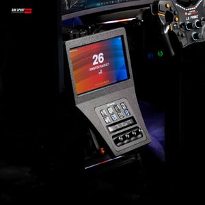 May include: A black sim racing dashboard display unit featuring a rectangular screen showing the number 26 and the text SIMSPORTGADGET. Below the screen is a control panel with eight square buttons and four silver rotary knobs for racing settings.