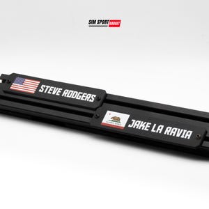 May include: Black metal nameplates with white text that reads "STEVE RODGERS" and "JAKE LA RAVIA". The "STEVE RODGERS" plate has an American flag graphic. The "JAKE LA RAVIA" plate has a California state flag graphic. The Sim Sport Gadget logo is in the top right.