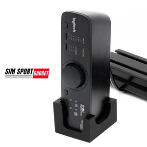 Peut inclure: Un mixeur audio Logitech G Pro X noir avec un grand bouton et plusieurs boutons. Le mixeur est sur un support noir et porte le texte "Logitech" et "DTS Headphone:X".