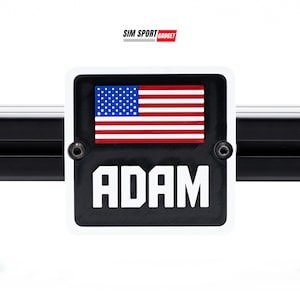 May include: A black and white rectangular nameplate with the name "ADAM" in bold white letters. The top of the nameplate features a small American flag. The nameplate is mounted with two screws. The Sim Sport Gadget logo is in the top corner.