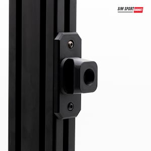 Op de afbeelding: Een zwart aluminium extrusieprofiel met een gemonteerde zwarte beugel met een centrale ronde opening. De beugel is bevestigd met twee zichtbare schroeven. De tekst SIM SPORT GADGET staat in de rechterbovenhoek van de afbeelding.