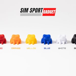 Pode incluir: Seis pequenas figuras de sapo em diferentes cores: vermelho, laranja, amarelo, azul, branco e preto. As figuras est&atilde;o dispostas em uma fileira sobre uma superf&iacute;cie branca. O texto "SIM SPORT GADGET" &eacute; exibido acima das figuras.