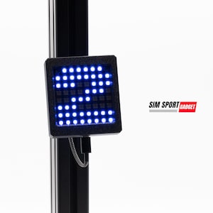 Puede incluir: Una pantalla LED cuadrada negra que muestra el número "2" en luces azules. La pantalla está montada en un poste negro. El texto "SIM SPORT GADGET" se muestra en blanco y rojo en el lado derecho de la imagen.