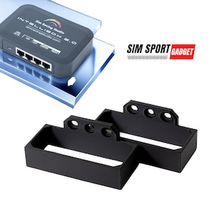 Puede incluir: Dos soportes de plástico negro impresos en 3D para montar un dispositivo. Los soportes tienen tres agujeros en la parte superior y una abertura rectangular en el medio.