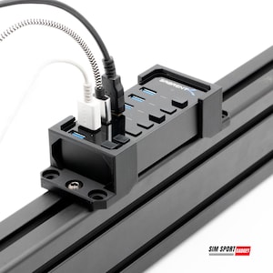 May include: A black USB hub with multiple ports and a "Sabrent" logo. Several USB cables are plugged into the hub, with a white and a black cable visible. The hub is mounted on a black metal frame.