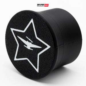 Könnte beinhalten: Schwarzes zylindrisches Objekt mit strukturierter Oberfläche. Die Oberseite zeigt ein weißes Sterndesign mit einem stilisierten Blitz im Inneren. Der Text "SIM SPORT GADGET" befindet sich in der oberen rechten Ecke.