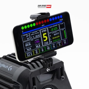 May include: A black smartphone mounted on a black racing simulator base, displaying a digital dashboard with telemetry data including RPM, engine temperature, fuel levels, and lap times. The screen shows the text SIM SPORT GADGET at the top.