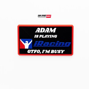 May include: Red and black rectangular patch with white text that reads "Adam is playing iRacing GTFO, I'm busy". The patch features a white silhouette of a race car driver with raised arms.