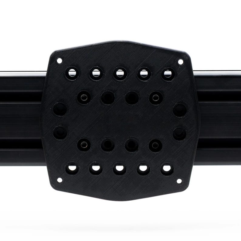 May include: A black, textured mounting plate with multiple holes and a curved shape, attached to a black metal rail. The plate has a series of circular and oblong holes. The background is white.