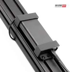 May include: A black electronic component with a rectangular body and a connecting cable, mounted on a black metal rail system. The text "SIM SPORT GADGET" is visible in the upper right corner. The component is likely part of a larger system.
