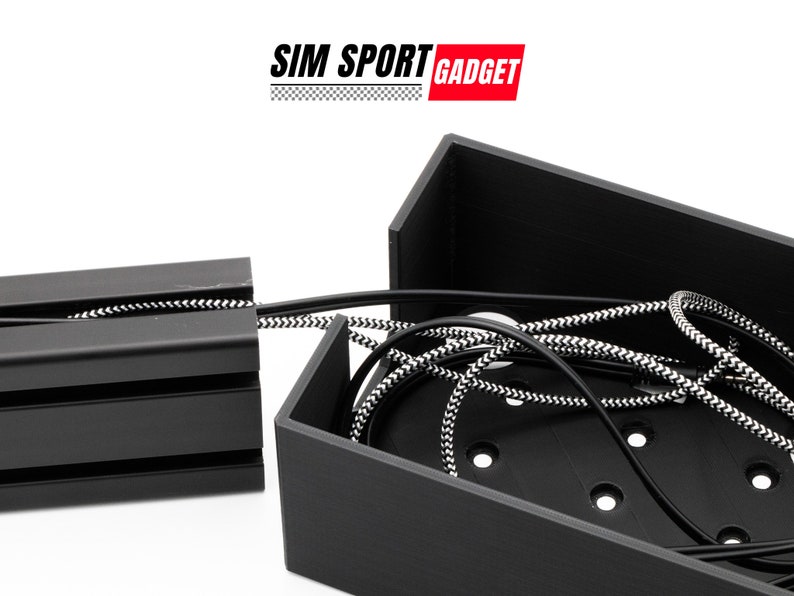 Pode incluir: Sistema de gest&atilde;o de cabos preto com um cabo tran&ccedil;ado preto e branco. O sistema tem uma base retangular com v&aacute;rios orif&iacute;cios e um canal para encaminhar cabos. O texto "SIM SPORT GADGET" &eacute; vis&iacute;vel no fundo.