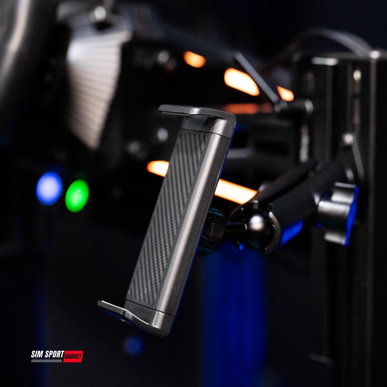 May include: A black and silver tablet holder with a carbon fiber pattern. The holder is mounted on a black adjustable arm. The text "SIM SPORT GADGET" is visible at the bottom.