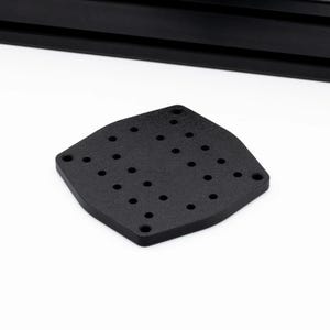 May include: A black, diamond-shaped metal plate with multiple evenly spaced holes. The plate has a textured surface and rounded edges. A black, rectangular object is visible in the background.