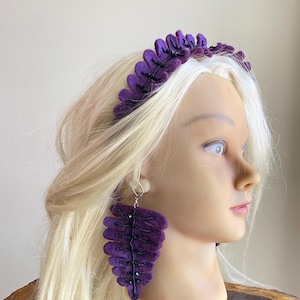 May include: A purple felt headband and matching earrings. The leaf-shaped headband and earrings are decorated with black beads. The earrings hang from silver hooks. The jewellery is displayed on a mannequin head with blonde hair.