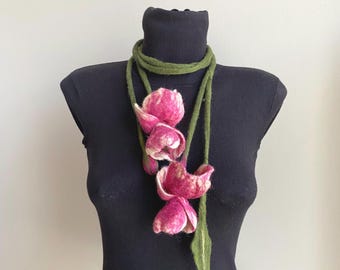May include: A handmade felt necklace featuring three pink and white flower blossoms with green stems and a green cord. The necklace is displayed on a black mannequin.