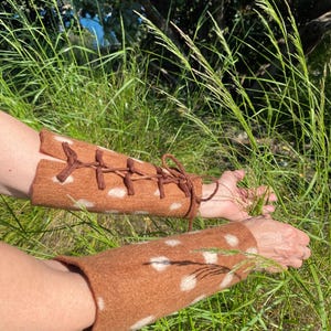 May include: A pair of brown and white spotted arm warmers with brown laces. The arm warmers are made of a soft, fuzzy material and are perfect for keeping your arms warm in the winter.