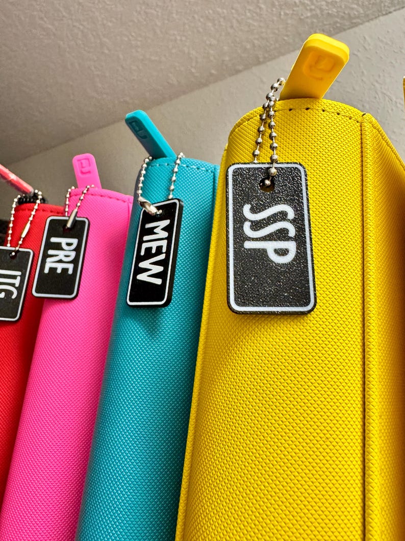 May include: Four colorful zippered pouches with black and white labels hanging from a shelf. The labels read "TIC", "PRE", "MEW", and "SSP".