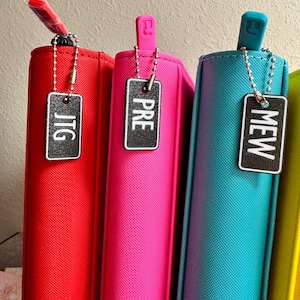 May include: Four colorful binders with zipper pulls and metal keychains with tags that read "JTG", "PRE", "MEW", and an unreadable word. The binders are red, pink, blue, and yellow.