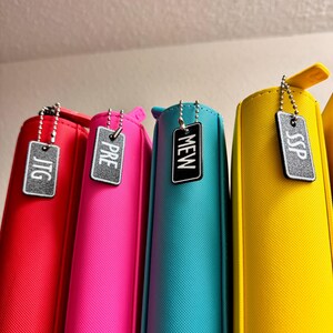 May include: Four colorful zippered pouches with metal zipper pulls and attached tags. The tags are rectangular and have the words "JTG", "PRE", "MEW", and "SSP" printed on them in white.