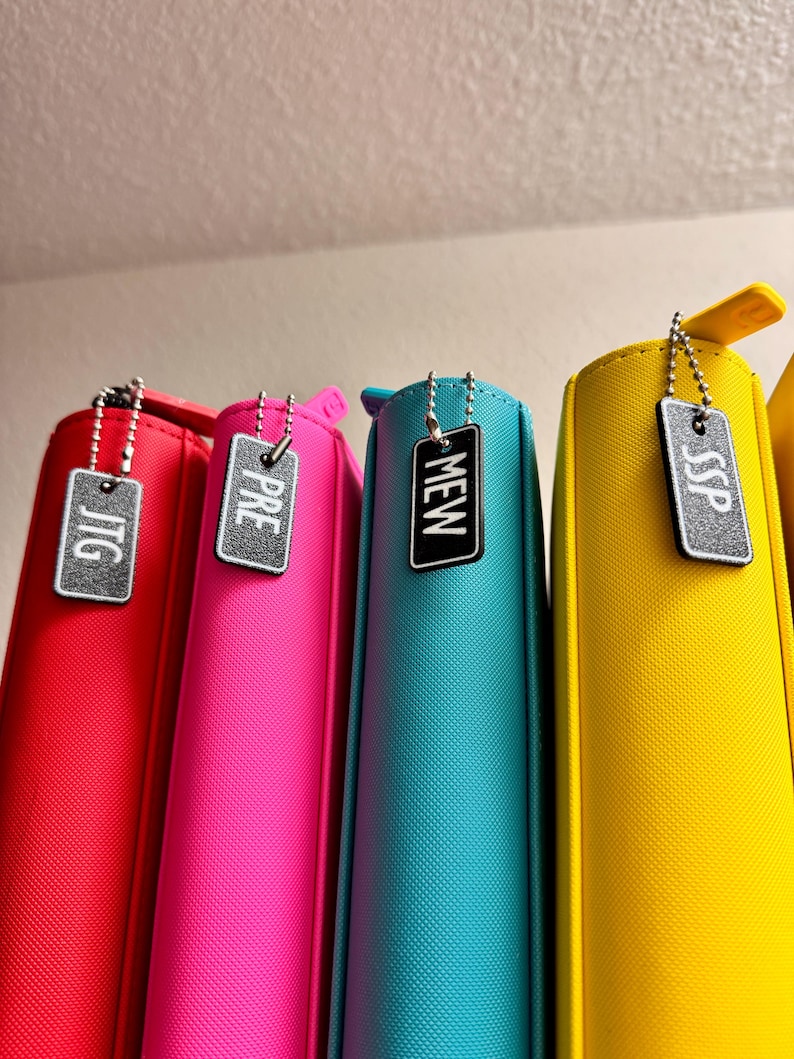 May include: Four colorful zippered pouches with metal zipper pulls and attached tags. The tags are rectangular and have the words "JTG", "PRE", "MEW", and "SSP" printed on them in white.
