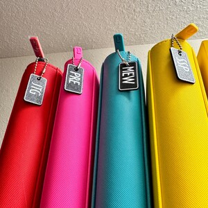 May include: Five colorful zippered pouches with silver keychains and tags that say "JTG", "PRE", "NEW", "SSP".
