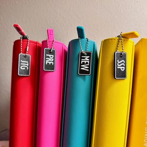 May include: Five colorful zippered binders with black metal tags labeled "JTG", "PRE", "MEW", "SSP", and "SIDE LOADING 11"