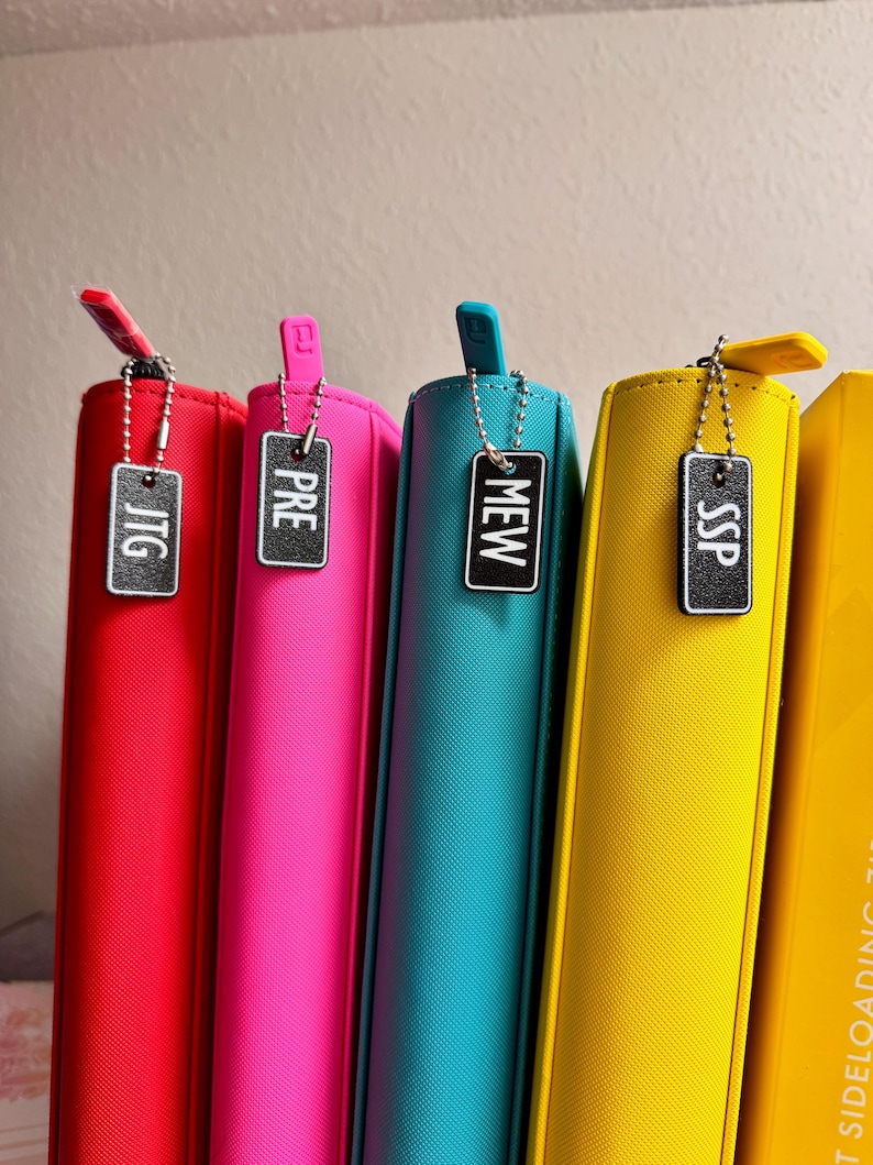 May include: Five colorful zippered binders with black metal tags labeled "JTG", "PRE", "MEW", "SSP", and "SIDE LOADING 11"