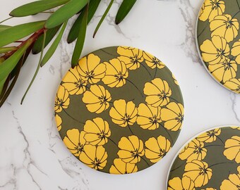 Könnte beinhalten: Drei runde Untersetzer mit einem Blumenmuster. Die Untersetzer zeigen gelbe Blumen auf einem dunkelgrünen Hintergrund.