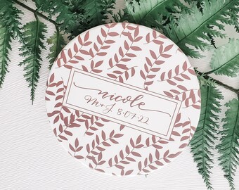 May include: A white round box with a brown leafy pattern and the text "nicole M+J 8.07.22" in a brown rectangle.