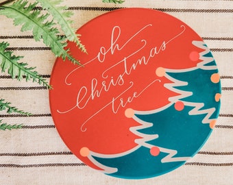 Könnte beinhalten: Ein runder Untersetzer aus Keramik in Rot und Blau mit einem weißen Design, auf dem "oh christmas tree" steht.