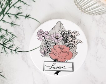 May include: White round coaster with a floral design featuring pink and peach flowers, green leaves, and the name "Susan" written in cursive.